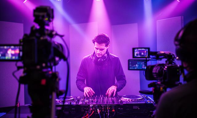DJ actuando en una sesión musical grabada con iluminación violeta y cámaras de estudio